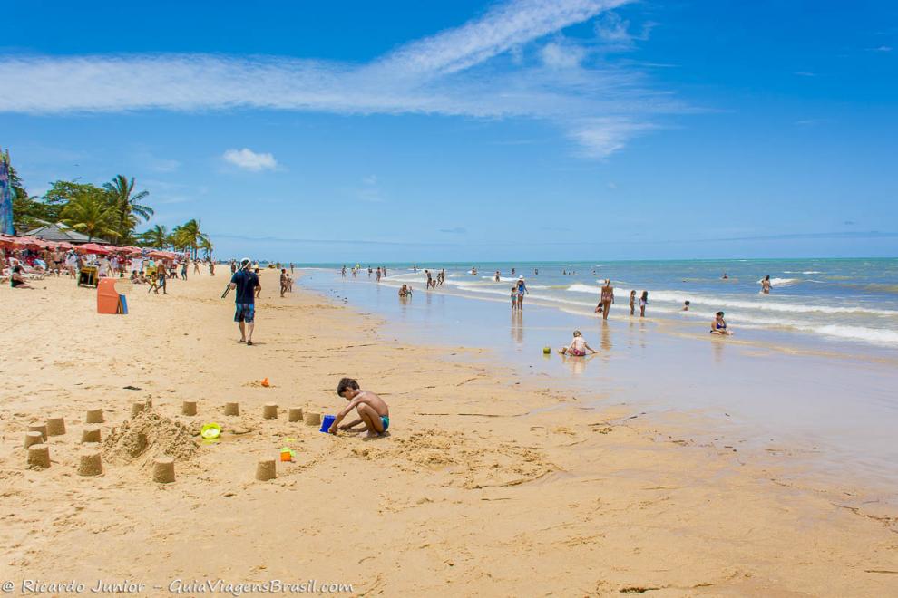 Imagem de um menino fazendo vários castelinhos de areia na beira do mar.